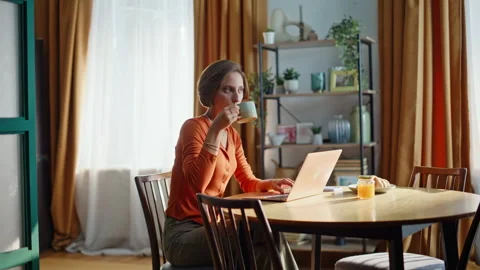 Remote worker drinking coffee sitting kitchen table with laptop. Pensive woman Stock Footage 333382896