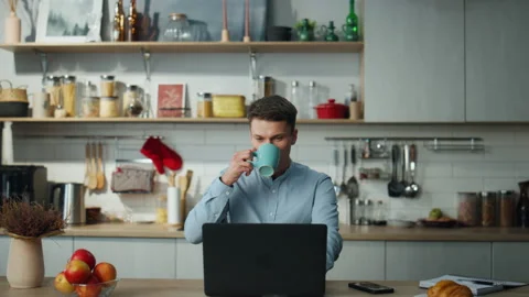Remote worker drinking coffee working on laptop from home. Man feeling relaxed. Stock Footage 227589423