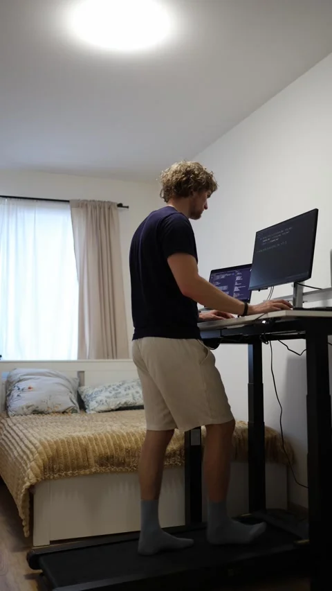 Remote worker lowers adjustable desk while walking on treadmill at home Stock Footage 346881267