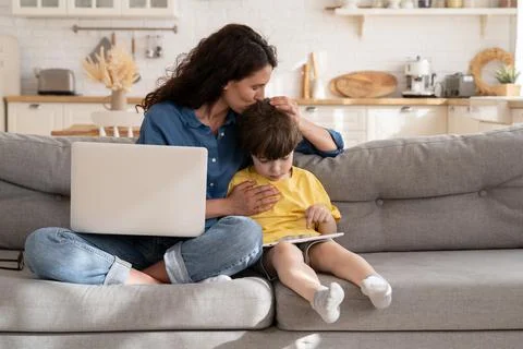 Remote worker mom or freelancer embrace kid with tablet using laptop computer to Stock-Fotos
