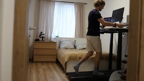 Remote worker runs on treadmill while working at computer in home office Stock Footage 347269930