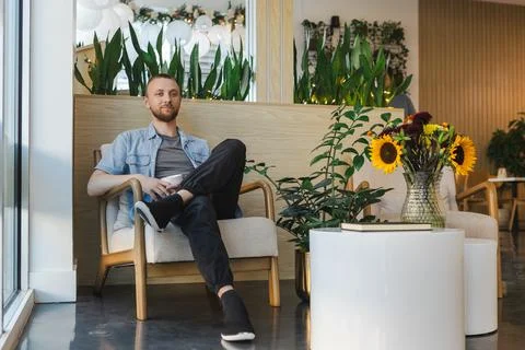 Remote worker sits in a cafe with plants and flowers, focused on online tas.. Фото
