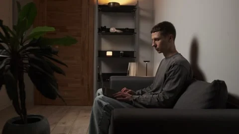 Remote worker sitting on a cozy sofa at home, working on a laptop in a warm Stock Footage 315665866