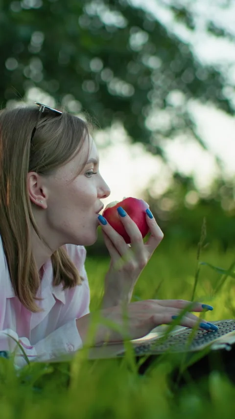 Remote Worker Typing on Laptop While Relaxing Outdoors with Apple in Hand Stock Footage 317584131