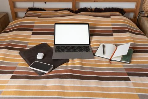 Remote workspace setup on a bed with a laptop mockup and a smartphone 写真素材