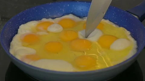 Removing bubbles with a knife while frying eggs in a frying pan on the hob Stock Footage 138317258