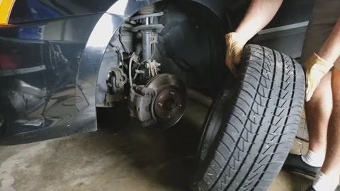 Removing front left wheel and tire from sedan car exposing axle assembly Video stock 129864937