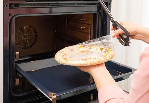 Removing the packaging from the pizza before placing it in the oven Stock-Fotos