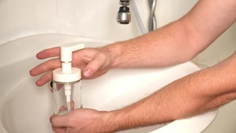 Removing pump to fill container. A man opens glass soap dispenser to pour soap Stock Footage 244789951