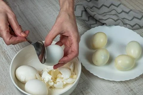 Removing the shell from boiled white eggs. A housewife takes an iron spoon .. Stock Photos
