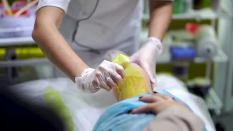 Removing a strip of yellow sugaring paste from the leg of a woman lying on table Stock Footage 257251343