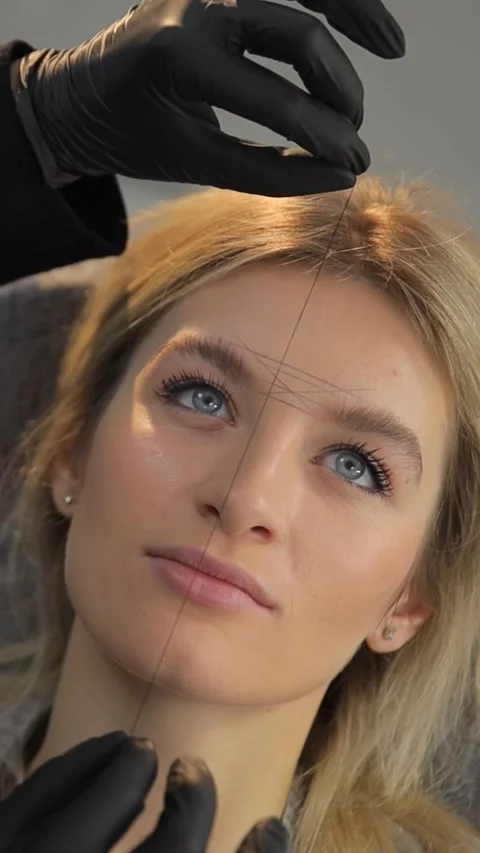 Removing unwanted hair from the eyebrows with a thread, a cosmetologist does Stock Footage 263052710