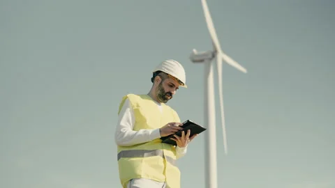 Renewable energy engineer uses a tablet to audit wind turbines in a field Stock Footage 234191320