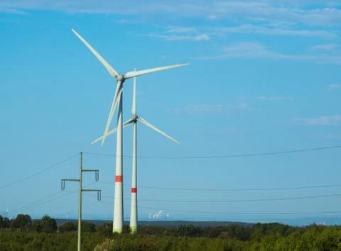 Renewable energy generated by two windmills with power plant in background Stock Photos