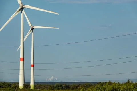 Renewable energy generated by two windmills with power plant in background Stock Photos