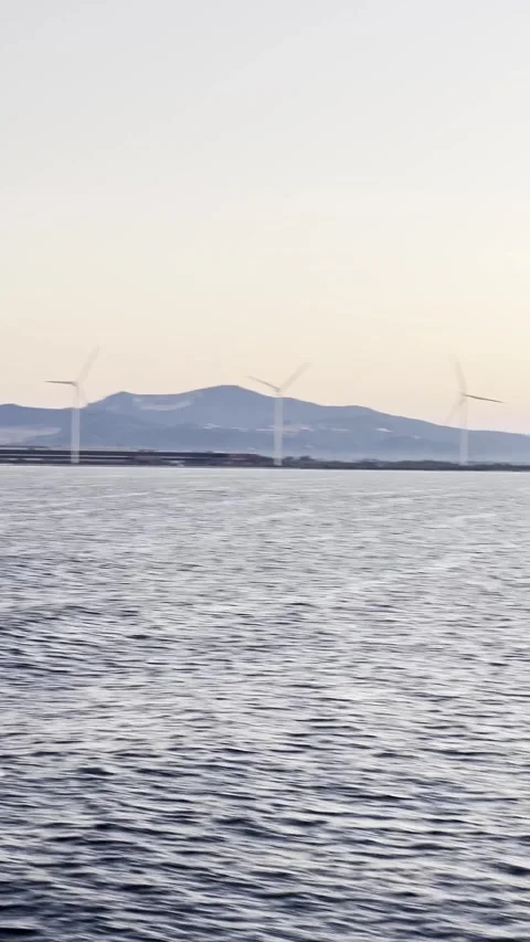 Renewable energy wind farm beyond coastal waters at dusk Stock Footage 334807919