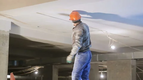 Repair inside the building. Worker in the mask plaster ceiling standing on high Stock Footage 115862702