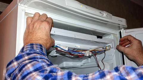 Repairing a refrigerator with complex wiring inside a kitchen setting durin.. Фото
