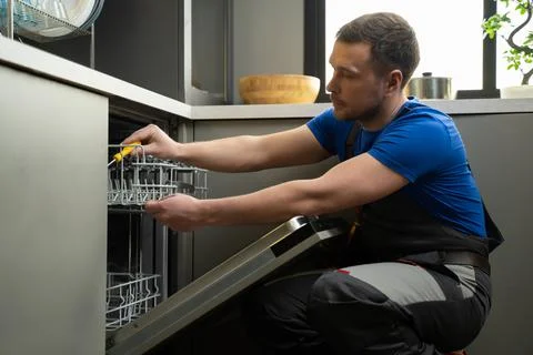 Repairman checks operating state of dishwasher in kitchen Stock Photos