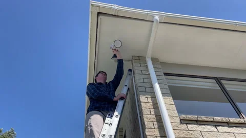 Repairman installing a double LED light on the corner of a 1980's house Vídeo Stock 289038084