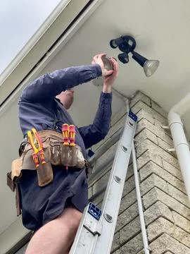 Repairman installing a double LED light on the corner of a 1980's house Stock Photos
