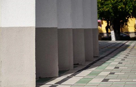 Repeating architectural concrete pillars casting shadows on paved city square Stock Photos