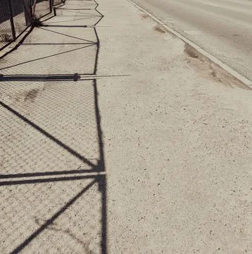 Repeating fence shadows form a pattern across an outdoor pavement surface. Stock Photos