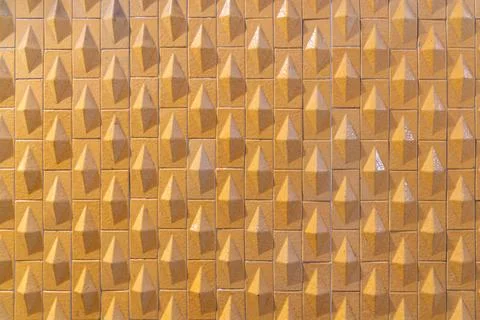 Repeating triangular relief pattern on yellow textured tile surface Stock Photos