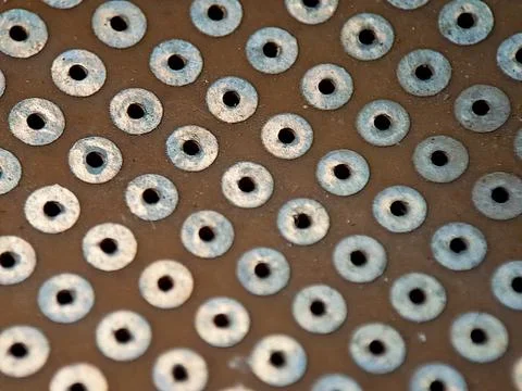 A repetitive pattern of metallic washers uniformly adorns a textured brown .. Stock Photos