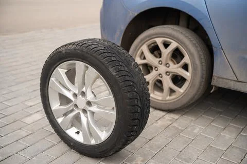 A replacement winter wheel stands next to a blue car Stock Photos