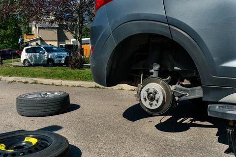 Replacing a flat tire roadside: car with missing wheel on a sunny street. Stock Photos