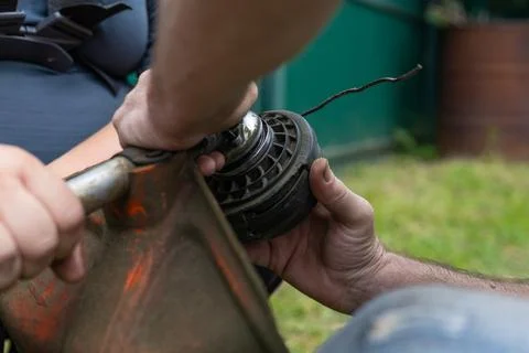 Replacing the nylon thread on a grass trimmer. A man unscrews the nut to change 스톡 사진