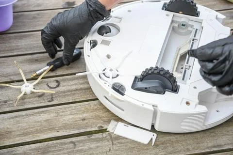 Replacing a worn brush on a robot vacuum cleaner, a woman unscrews Stock Photos
