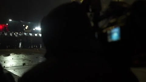 A reporter with a camera for broadcasts a protest, with crowd of police in frame Video stock 297994800