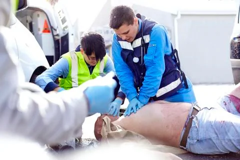 Rescue workers performing CPR on car accident victim in road Foto stock