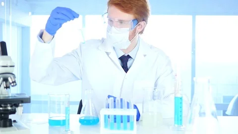 Research Scientist Looking at Blue Solution in Test Tube in Laboratory Stock Footage 80944786