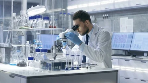 Research Scientist Looks into Microscope and Writes Down Observations.  Video stock 75403619