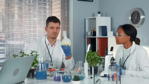 Research scientist providing experiment with liquid in flask while his collegue Stock Footage 115251674