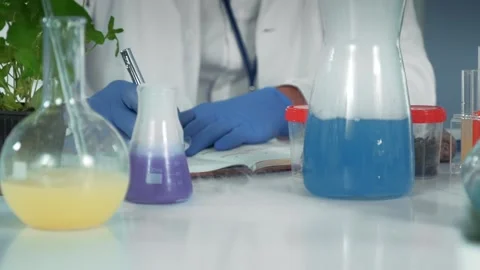 Research scientist writing notes at laboratory table with chemical flasks Stock Footage 340986393