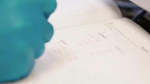 Researcher in science lab writes notes in book 스톡 동영상 129919463