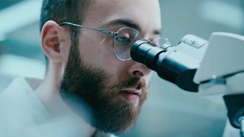 Researcher Using Microscope and Speaking with Assistant in Laboratory Stock Footage 331337754