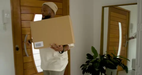 Resident receiving delivery, carrying box through front door, placing on coffee Stock Footage 341932774