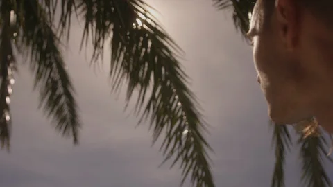 Resort Package 132 | closeup man walking sun shining through palms next to pool Stock Footage 118525583