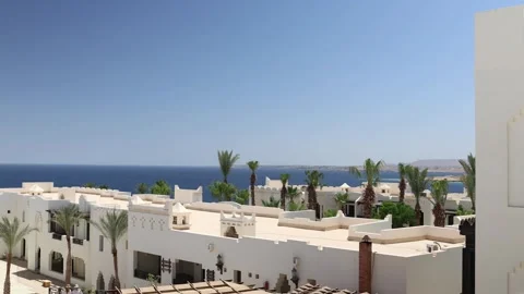 Resort rooftops with white geometric facades and tall palm trees overlook the de Stock Footage 310537091