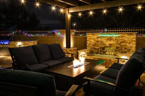 A resort style backyard at night with a waterfall, pergola, and a firepit Stock Photos