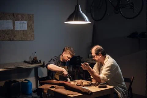 A respectable elderly shoemaker conducts a master class for a young boy on Stock Photos