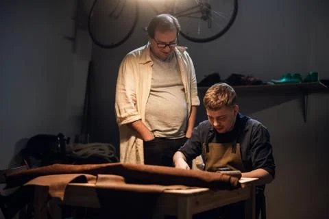 A respectable elderly shoemaker conducts a master class for a young boy on Stock Photos