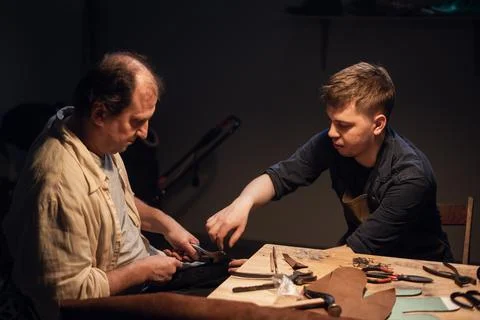 A respectable elderly shoemaker conducts a master class for a young boy on Stock Photos