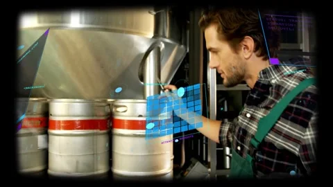 Responding to holo overlay, tech in green overalls checking kegs and noting on Stock Footage 334182749