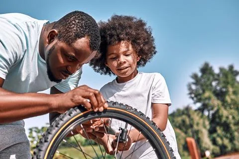 Responsible father fixing a flat tyre of his son bike Stock Photos